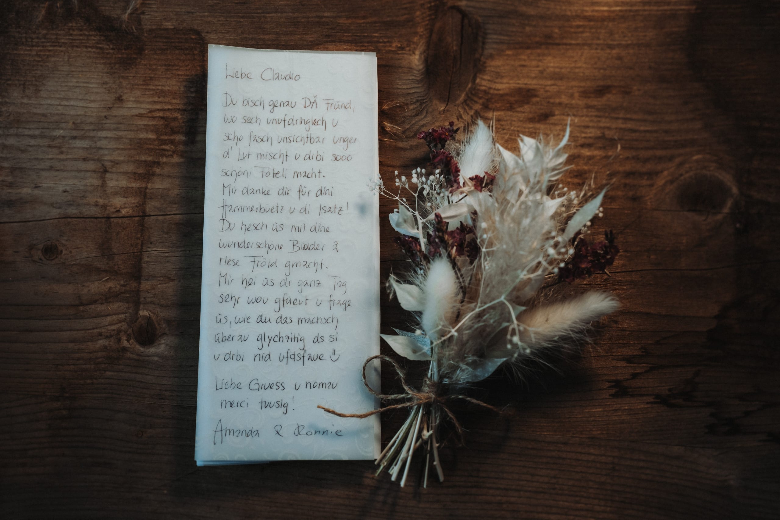 Handgeschriebene Dankeskarte eines Brautpaars auf einem Holztisch, daneben ein Strauss Trockenblumen