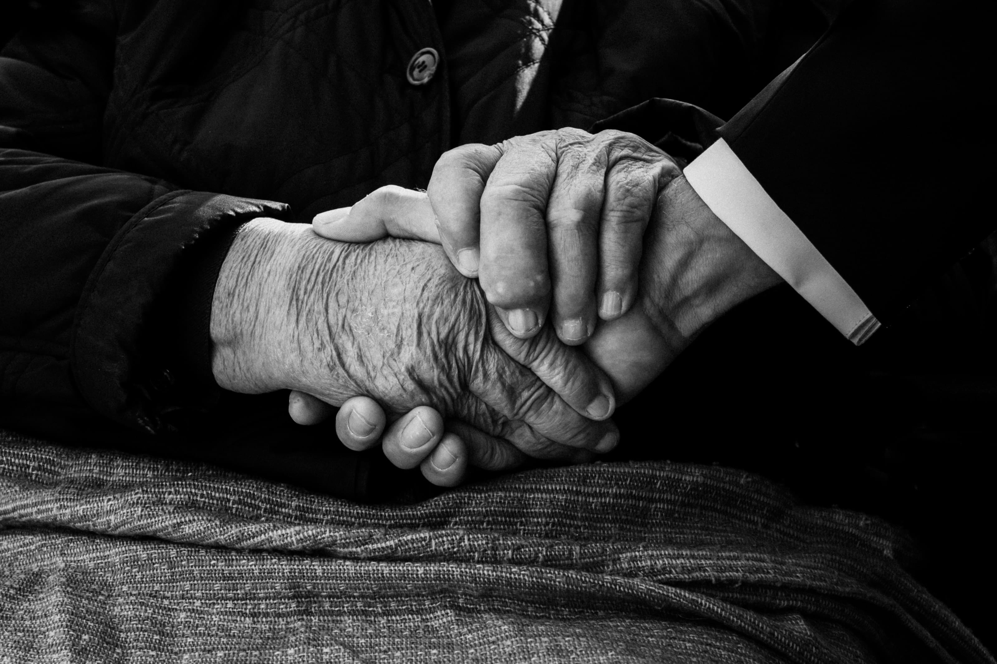 Schwarzweissfoto: Zwei alte Hände umfassen die Hand eines Mannes im Anzug